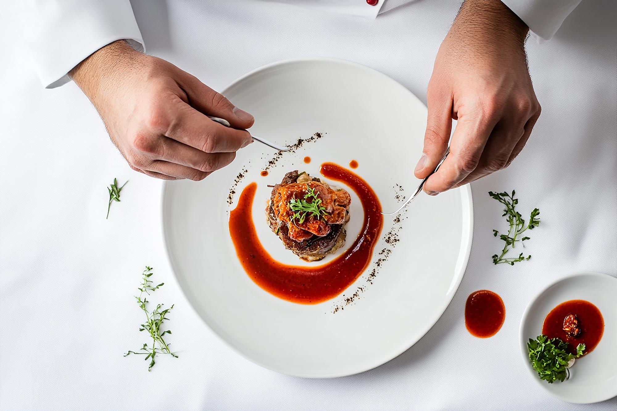 Chef plating a refined dish on dark table